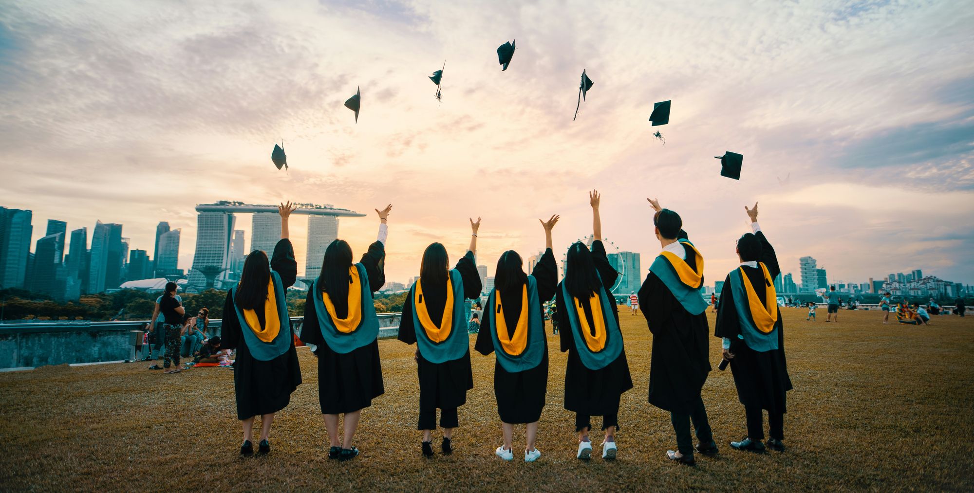 Graduates throwing their caps into the air at sunset with a city skyline behind them